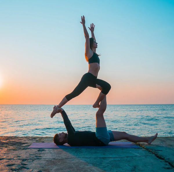 Couple performing acro yoga at sunset by the sea, highlighting Ayra Energy’s commitment to well-being and conscious living.